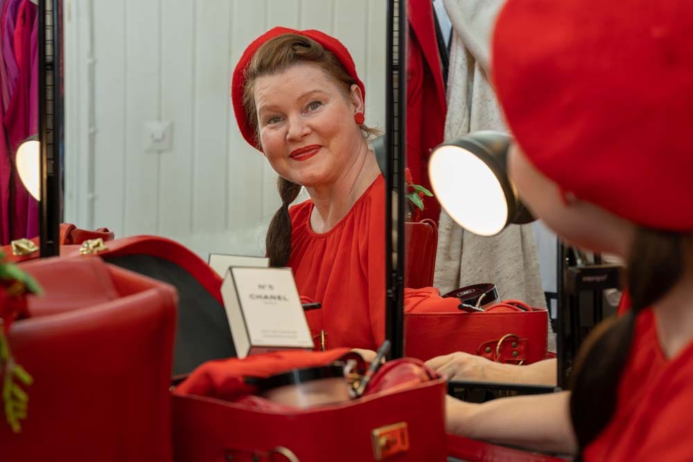 Stylisti Mia Frilander peilin edessä punaisissa asusteissa ja vintage-laukkujen ympäröimänä.